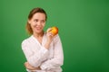 A good-looking woman of forty in a white shirt on a green background smiles and holds a fresh apple in her hands. Healthy eating, Royalty Free Stock Photo