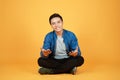 Good looking young Asian man sitting with legs crossed on the floor, isolated on orange background Royalty Free Stock Photo