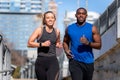 A good looking young athletic couple running through the city in urban lifestyle active sport portrait, buildings in background