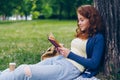 Good-looking young lady reading book and smiling sitting on lawn in park Royalty Free Stock Photo