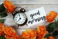 Good Morning card and alarm clock with orange flower decoration on wooden background Royalty Free Stock Photo