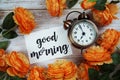 Good Morning card and alarm clock with orange flower decoration on wooden background Royalty Free Stock Photo