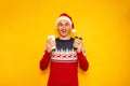 Good morning on Christmas Eve, excited man in sweater with reindeer red Santa Claus hat holds paper cups for hot drinks