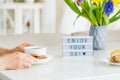 Good morning concept, breakfast time. Close up woman with cup of hot coffee drink, cookies, lightbox with message Enjoy your day