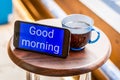 good morning digital text in blue smartphone screen with a glass of tea on brown wooden table Royalty Free Stock Photo