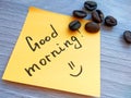 Good morning handwritten message on orange sticky note with coffee beans on wooden background