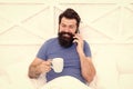 Good morning. Hello dear. Bearded man using mobile technology in bed. Handsome guy talking on phone and drinking coffee Royalty Free Stock Photo