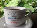 Good morning. Make great things happen today. Morning motivational text message on a cup of coffee on the table.