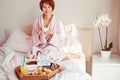 Good morning mood. Young woman in bathrobe sitting on the bed, drinking coffee and has her breakfast in bed with Have a nice day