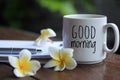 Good morning text greeting on a cup of morning coffee with Bali frangipani flowers, paper work on desk  and an happy smile Royalty Free Stock Photo