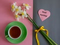 Good morning wishes note in shape heart, tea cup and white yellow daffodils bouquet on pink and grey paper background Royalty Free Stock Photo