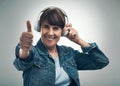Good music just gets you. Studio portrait of a senior woman showing thumbs up while wearing headphones against a grey