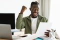 Good news. Overjoyed black man reading letter, raising fist and exclaiming with excitement, sitting at home office Royalty Free Stock Photo