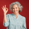 Good, perfect and okay with a senior woman hand gesture or sign in support or positive backing in studio against a red