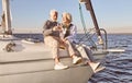 Good vibes. Happy senior couple sitting on the side of sail boat or yacht deck floating in sea. Man and woman drinking Royalty Free Stock Photo