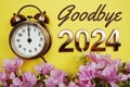 Goodbye 2024 text with alarm clock and flower decoration on yellow background