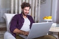 Goodlooking young man relaxing at home in armchair, sitting in living room with laptop computer, smiling. Typing new blog post. Royalty Free Stock Photo