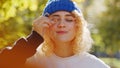 Goofy funny European young adult woman with blond, curly hair under a blue hat blinking her eyes and covering one eye Royalty Free Stock Photo