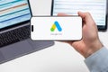 Google Ads logo on the screen of a cell phone in business mans hand and laptop on the background Royalty Free Stock Photo