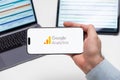 Google Analytics logo on the screen of a smartphone in mans hand with laptop and tablet with graphical diagrams Royalty Free Stock Photo