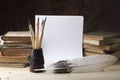 Goose feather and a glass with dirty brushes on the background of old books and sheets of white paper. Retro stylized photo Royalty Free Stock Photo