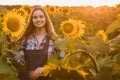 Gorgeous, adorable, female farmer standing in the middle of a beautiful green and golden sunflower field during a scenic sunrise Royalty Free Stock Photo