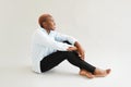 Gorgeous african american woman with short pink hair wearing white shirt and black jeans sitting on floor in studio on white Royalty Free Stock Photo