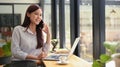 Gorgeous asian business woman having cell phone conversation while sitting front open laptop computer in coffee shop Royalty Free Stock Photo