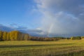 Gorgeous autumn colors landscape view.  Yellow field and forest trees. Rainbow in blue sky with blue clouds. Royalty Free Stock Photo