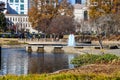 A gorgeous autumn landscape in the park with a still green lake and a water fountain in the center of the lake