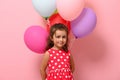 Gorgeous baby girl wearing summer polka dots dress, holding multicolored balloons behind her back, looking at camera. Happy Woman