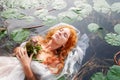 Gorgeous beautiful seductive portrait of a young sexy woman Ophelia with curly red hair lying with flowers with eyes closed dying