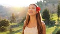 Gorgeous beautiful young woman with long hair and red flower on ear enjoying breathing fresh air in nature. Pretty smiling girl Royalty Free Stock Photo