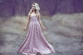 Gorgeous blond lady with luxuriant hairstyle in long brocade dress walking along the narrow path in the woods Royalty Free Stock Photo