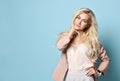 Girl in beige jacket and white overall. Smiling, folded her hands, posing standing against blue studio background. Close-up