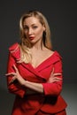 Blonde girl with deep neckline, hands folded, in red dress and black earrings. She looking at you, posing on gray Royalty Free Stock Photo