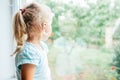 A gorgeous blonde little girl with ponytale staring out of the window on a wet, cold rainy summer day Royalty Free Stock Photo