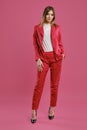 Blonde model in red pantsuit, white blouse, high black heels. Posing standing against pink studio background. Beauty Royalty Free Stock Photo