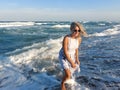 Gorgeous blonde woman in white dress on the beach with sea waves