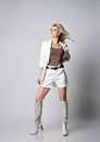 Gorgeous blonde woman in white shorts, jacket and high boots for summer stands looking at upper corner Royalty Free Stock Photo