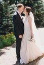 Gorgeous bride in amazing gown and stylish groom kissing and laughing in sunny park. Beautiful happy wedding couple enjoying time