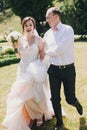 Gorgeous bride in amazing gown and stylish groom running and laughing in sunny park. Beautiful happy wedding couple enjoying time Royalty Free Stock Photo