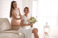 Gorgeous bride in beautiful wedding dress and her friend on sofa in room Royalty Free Stock Photo