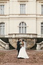 Gorgeous bride with bouquet and stylish groom walking at old castle in european city street in autumn time. happy wedding couple Royalty Free Stock Photo