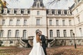 Gorgeous bride with bouquet and stylish groom walking at old castle in european city street in autumn time. happy wedding couple Royalty Free Stock Photo