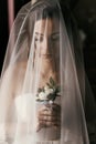 Gorgeous bride with boutonniere, posing under veil near window. amazing portrait of beautiful woman getting ready for wedding in