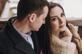 Gorgeous bride in coat and stylish groom gently hugging at old wooden house in winter forest. happy wedding couple embracing on Royalty Free Stock Photo