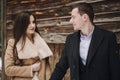 Gorgeous bride in coat and stylish groom posing at wooden house in winter forest. happy wedding couple gently hugging in snowy Royalty Free Stock Photo
