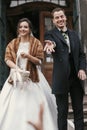 Gorgeous bride in coat and stylish groom throwing candy near church door after wedding ceremony.  happy newlywed couple smiling Royalty Free Stock Photo