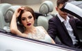 Gorgeous bride with fashion makeup and hairstyle in a luxury wedding dress with handsome groom near white cabriolet car Royalty Free Stock Photo